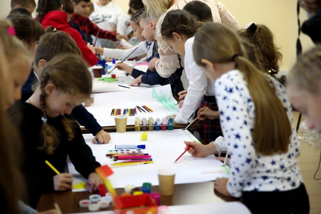 Niños y niñas pintando juntos sobre una mesa larga